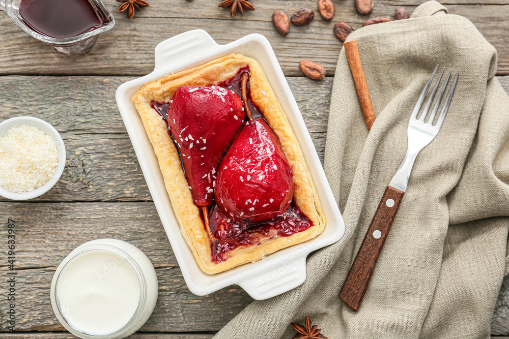 Baking dish of tasty poached pears in wine sauce on wooden background