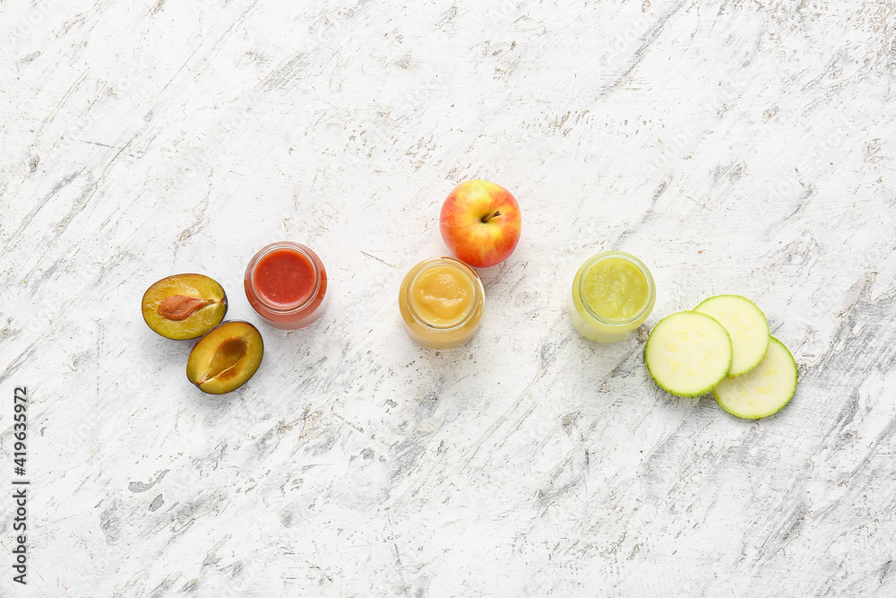 Jars with different baby food and ingredients on light background