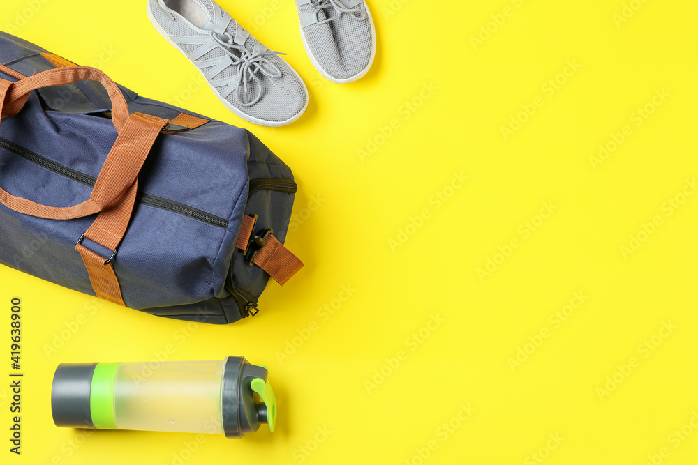 Sports bag, shoes and bottle of water on color background