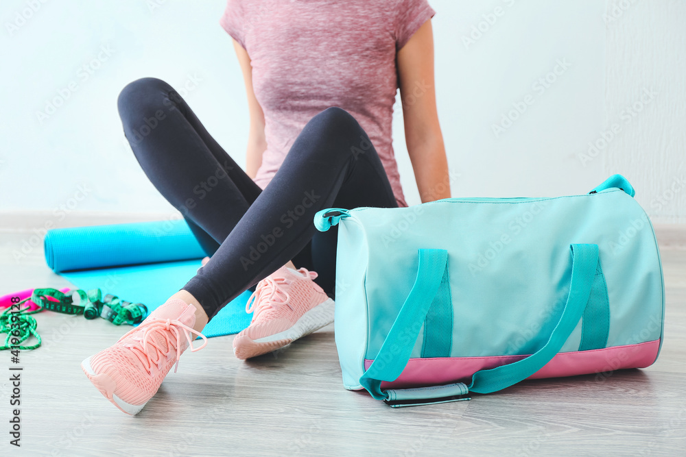 Young woman with sports bag and yoga mat in gym