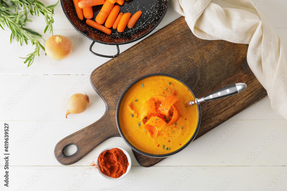 Cooking pot with tasty carrot cream soup on light wooden background