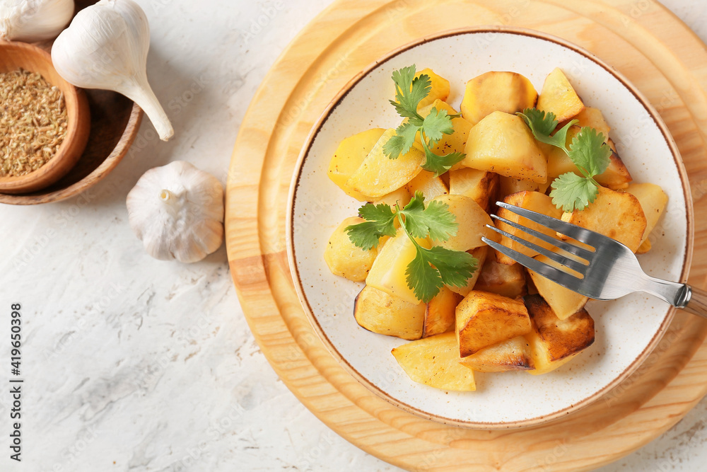 Plate of tasty baked potato with garlic on light background