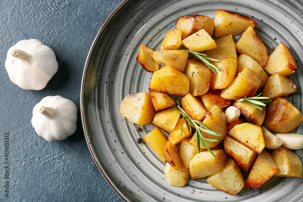 Plate of tasty baked potato with garlic on dark background