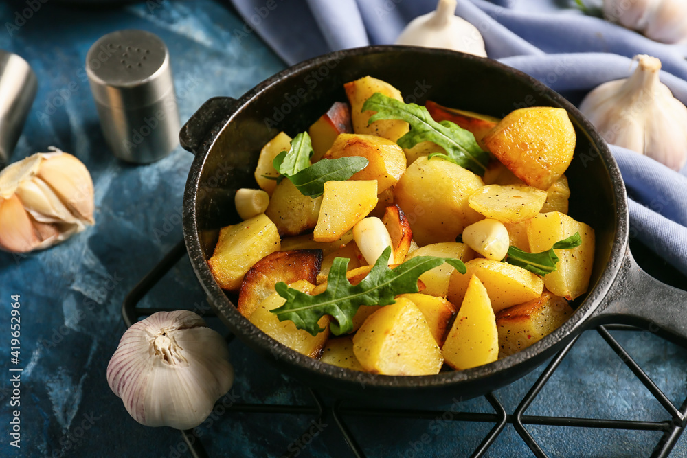 Frying pan of tasty potato with garlic on color background