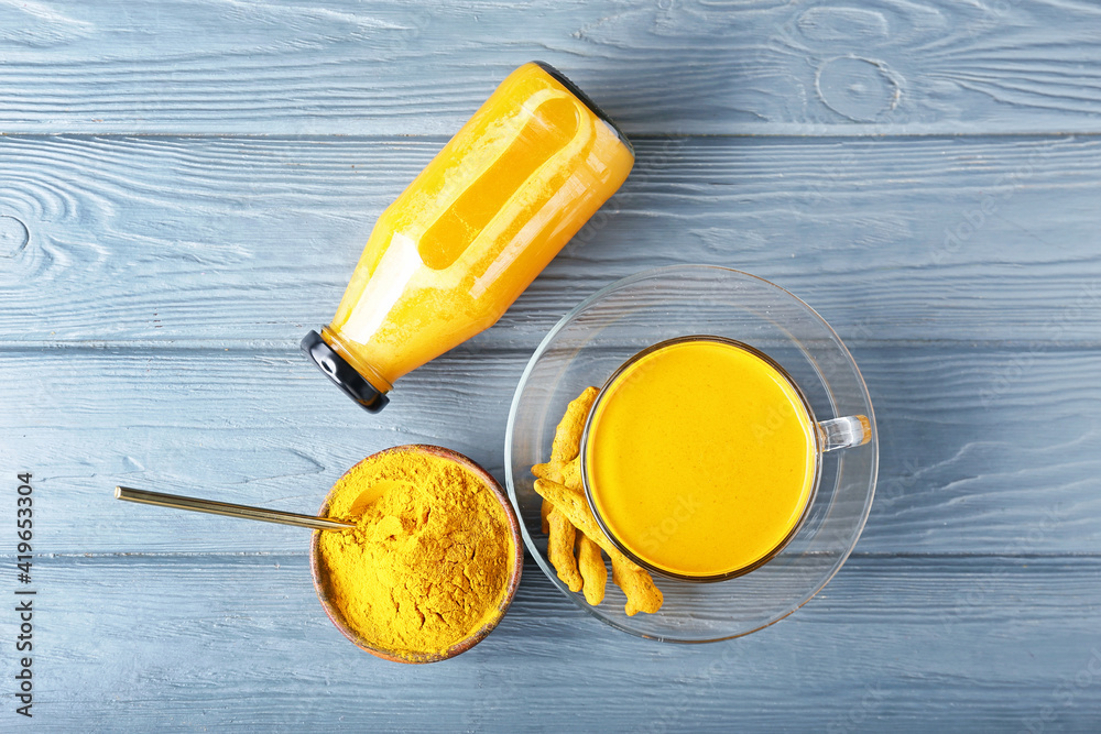 Cup and bottle of healthy turmeric drink on color wooden background