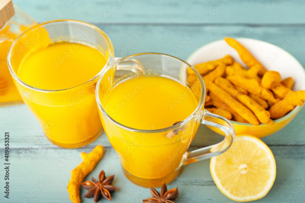 Cups of healthy turmeric drink on color wooden background