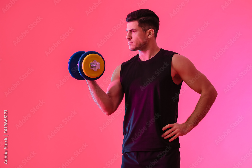 Sporty young man training with dumbbell on color background