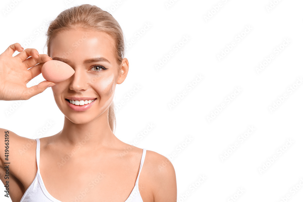 Beautiful young woman applying contouring makeup against white background