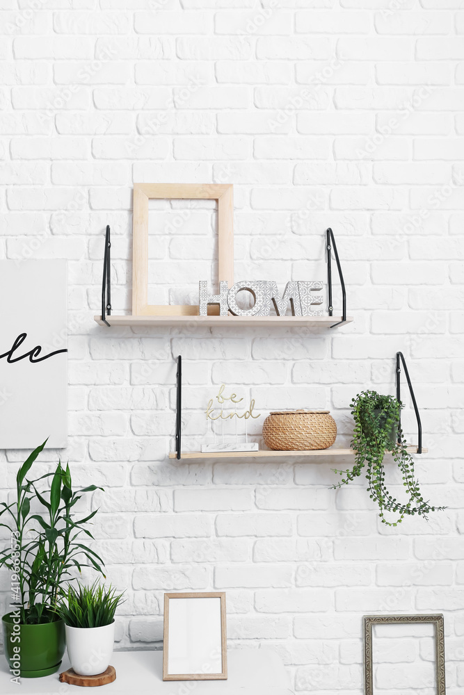 Shelves with stylish accessories and decor hanging on white brick wall