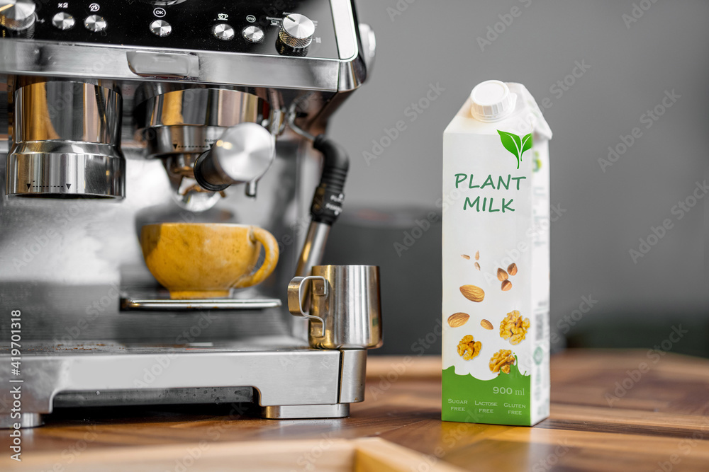 Packaging of vegetable milk near a cup of coffee and coffee machine on wooden table top on the kitch