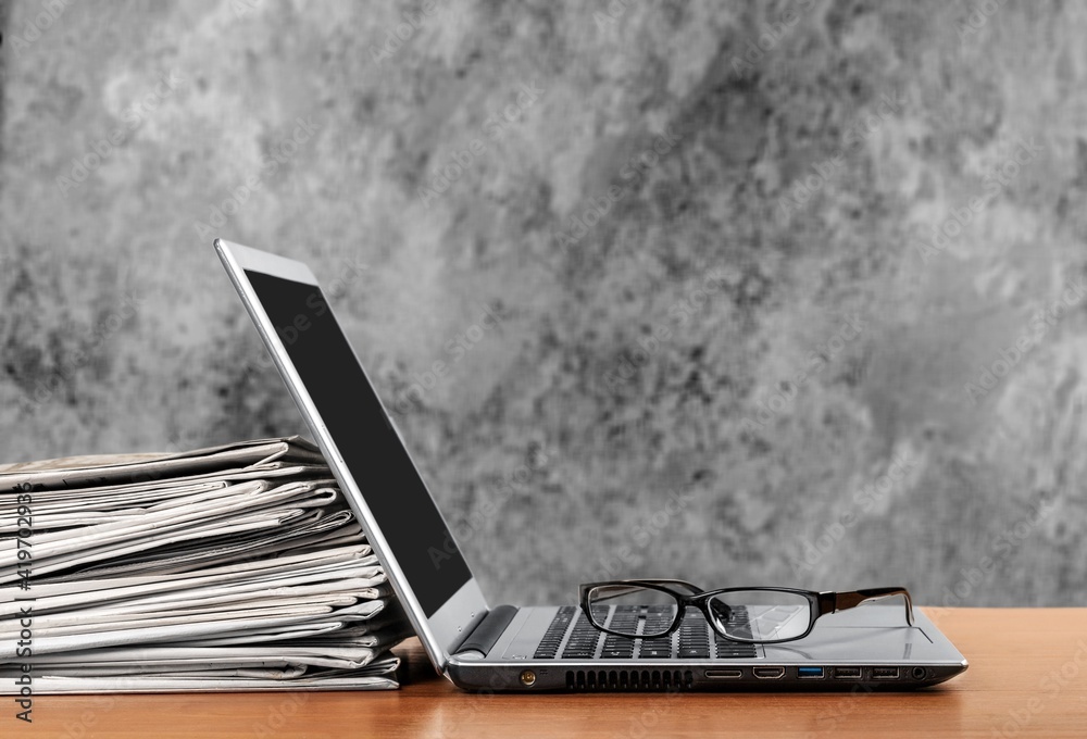 Laptop and newspapers stack on a table with background