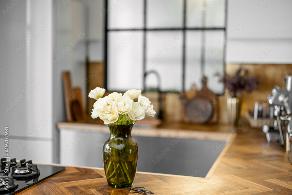 Vase with white flowers on stylish kitchen interior background with wooden table top. Home coziness 