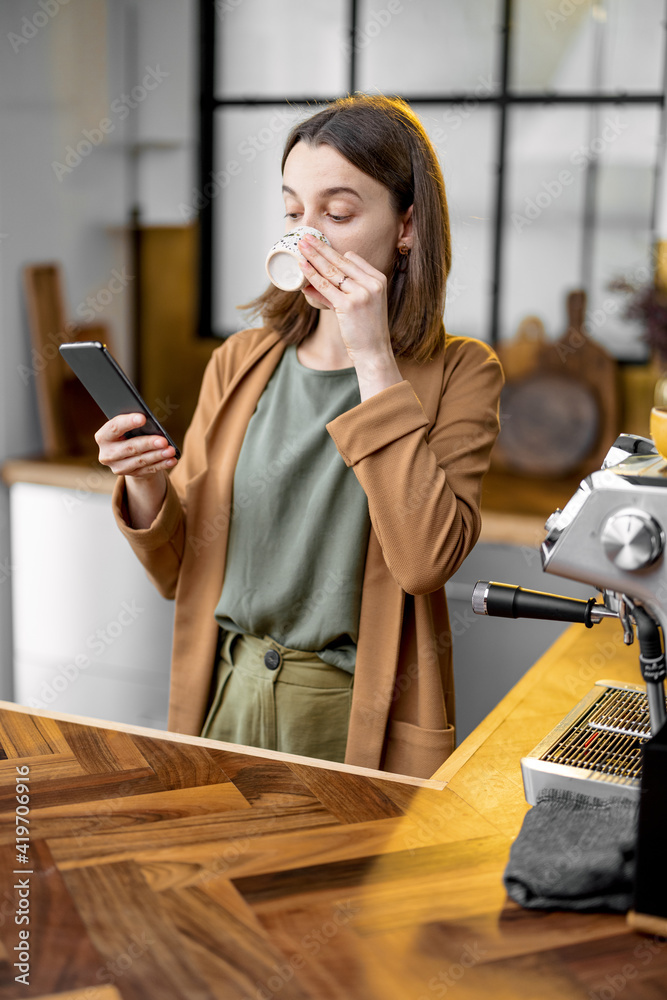 Fussy young woman in a hurry to work in the morning, wearing jacket, drinking coffee and chatting on