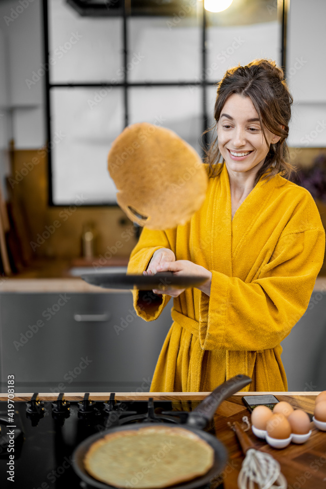 快乐的女人早餐做煎饼，在厨房里扔煎饼玩得很开心。很好