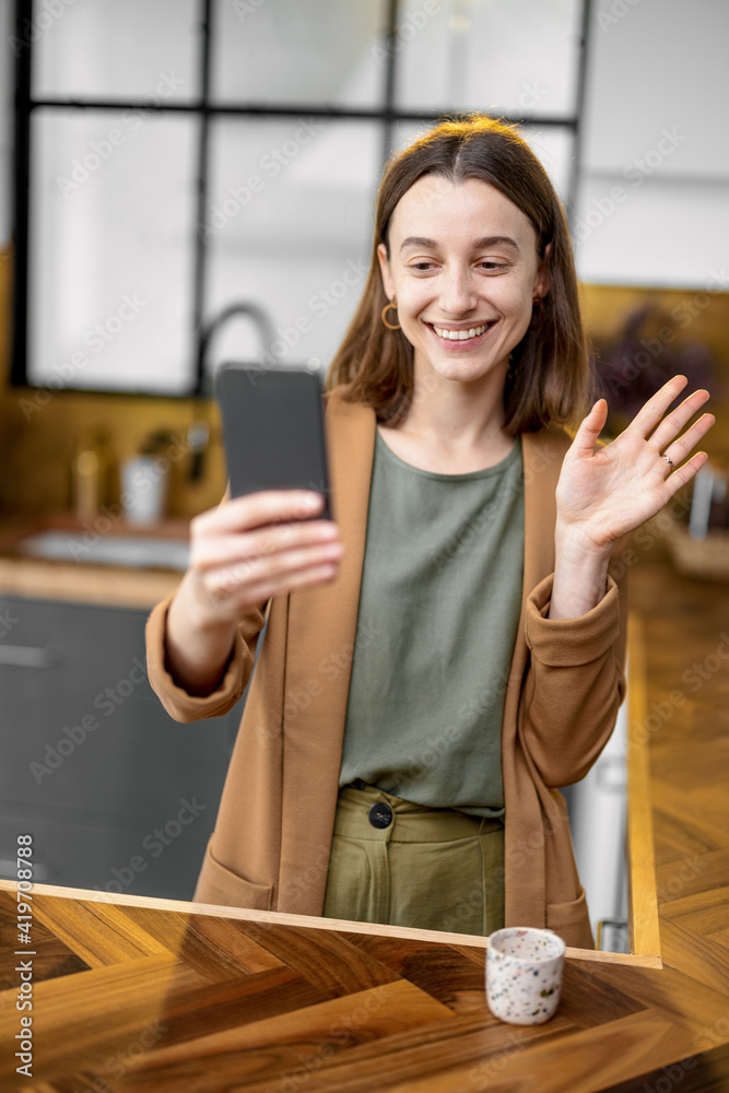 Pretty positive woman dressed in a brown jacket speaks and greets with hand on phone before the work