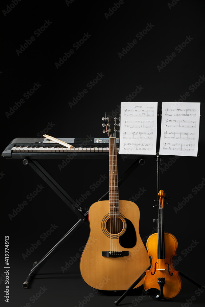 Note stand with music sheets and different musical instruments on dark background