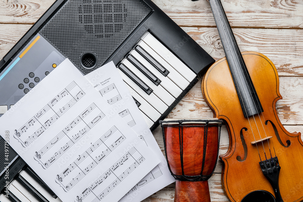 Different musical instruments and music notes on light wooden background, closeup