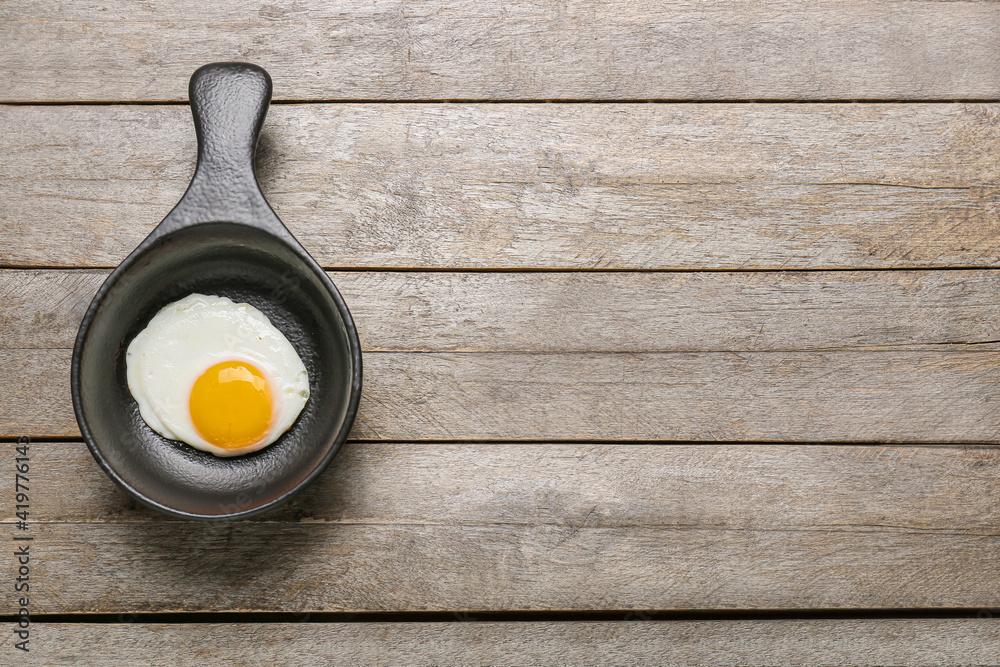 Frying pan with tasty egg on wooden background