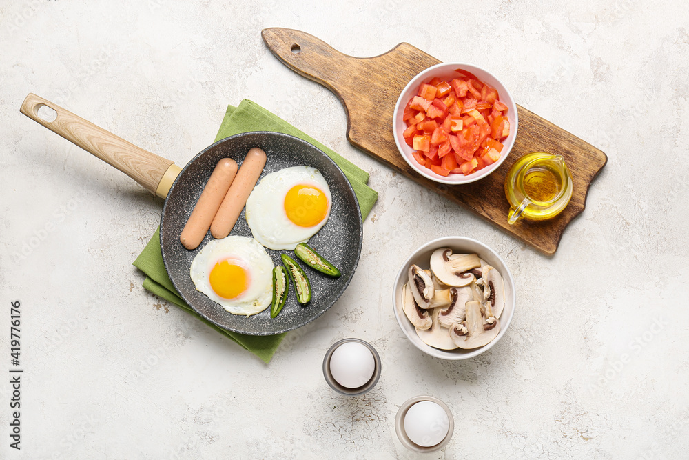 Frying pan with tasty eggs, sausages and pepper on table