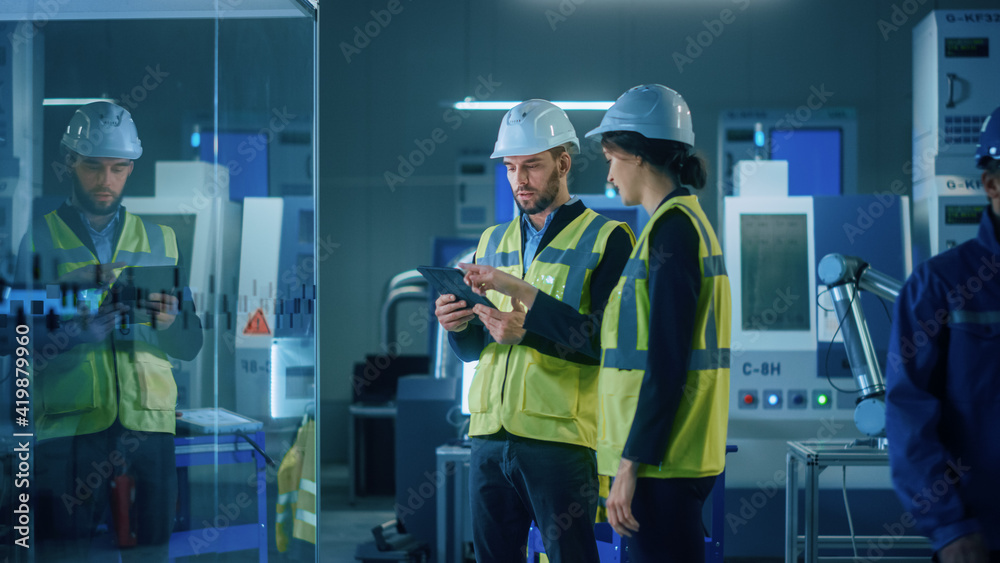 Modern Factory: Female and Male Engineers Wearing Safety Jackets, Hardhats Standing in Industrial Wo