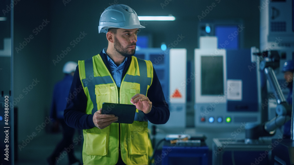 Professional Engineer Wearing Safety Vest and Hardhat Stands in Modern Factory Workshop, Uses Digita