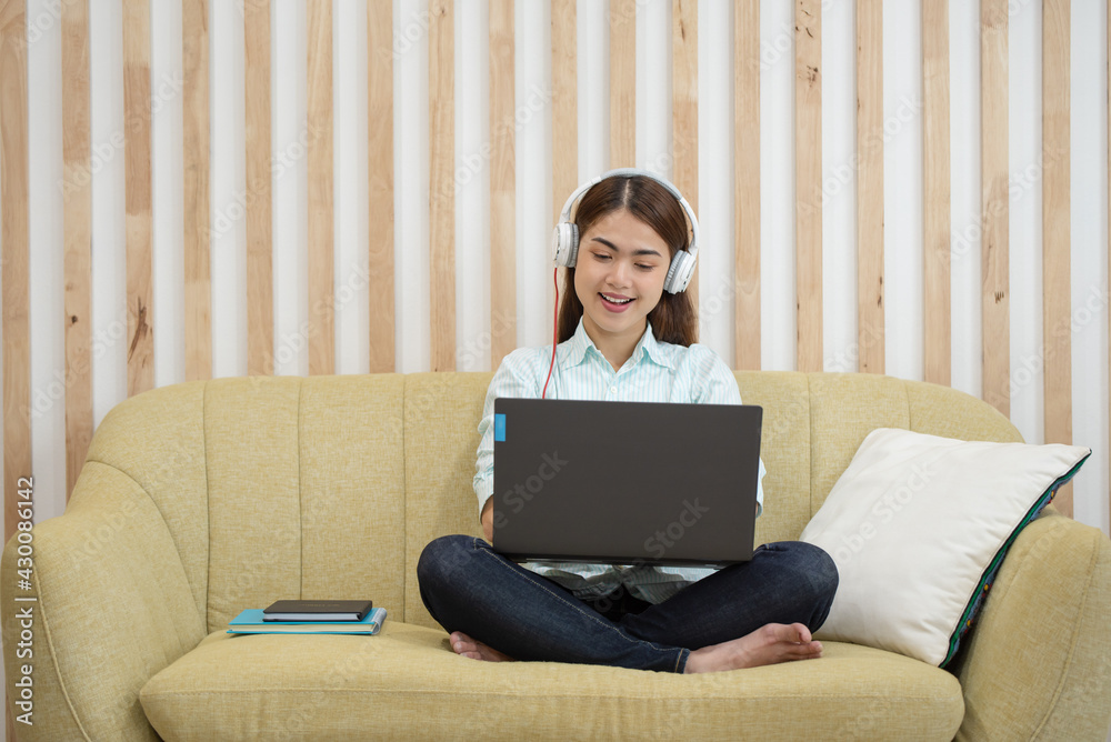 Happy young Asian woman listening to music with headphones relaxing at home