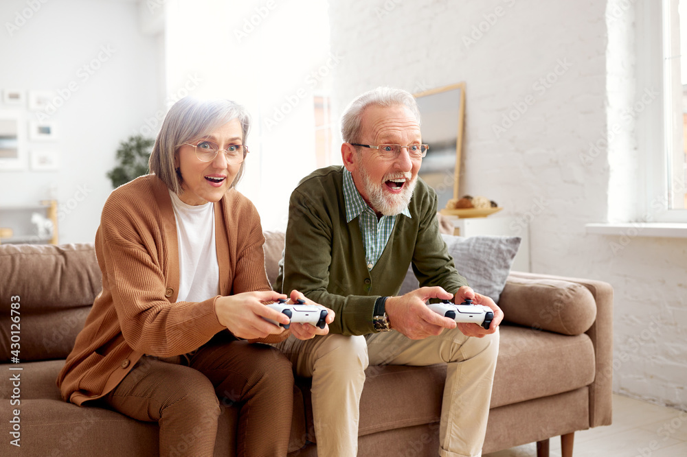 Excited senior couple playing video console games at home