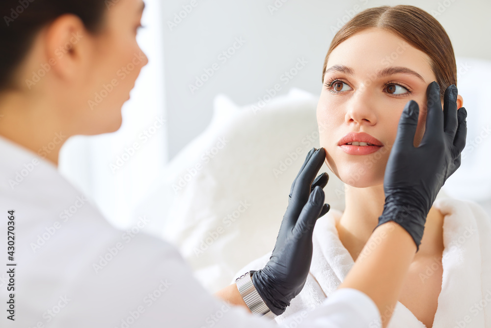 Cosmetologist in gloves checking face of woman