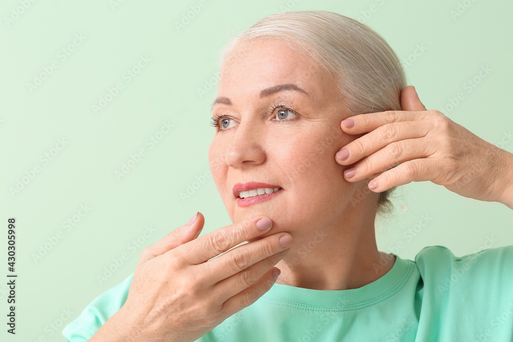 Mature woman giving herself face massage on color background