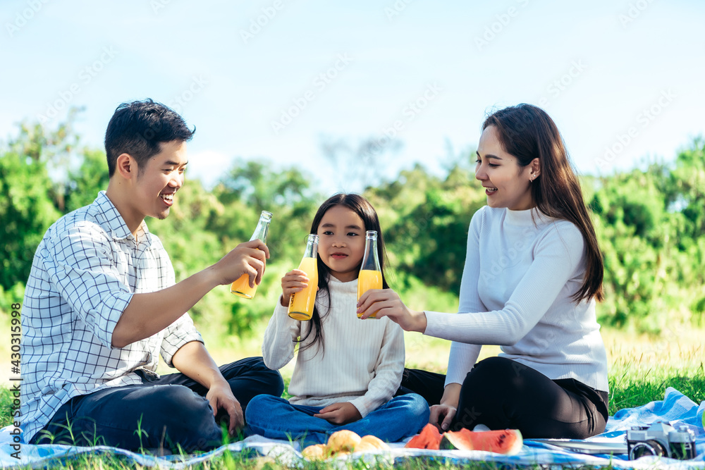 happy Asian family is having picnic in garden and drinking Orange juice in bottle with their daughte