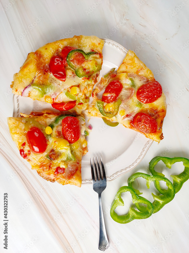 Three pieces of pizza in a white plate, fork, green pepper, white background, top view