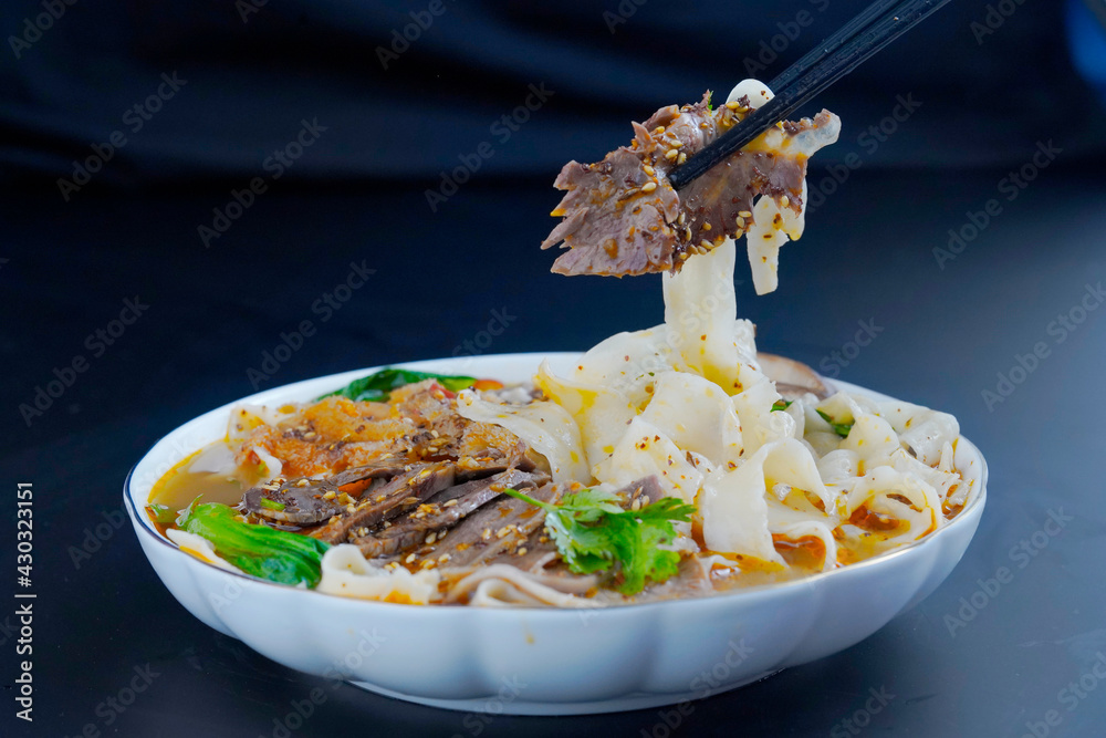 Close-up, someone picking up beef and noodles with chopsticks, black background