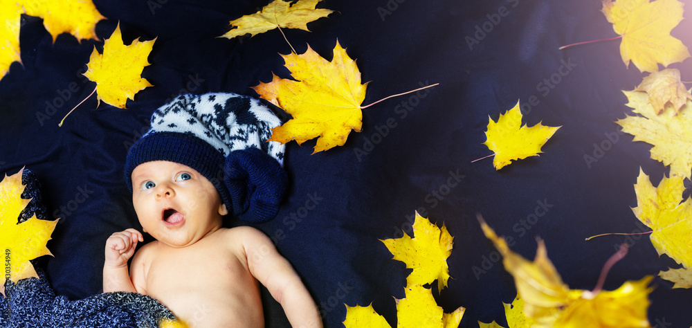 Newborn baby with autumn leaves in warm hat