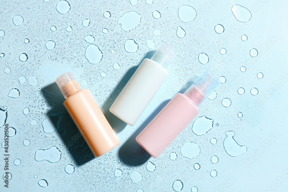 Bottles of cosmetic products on color background with water drops