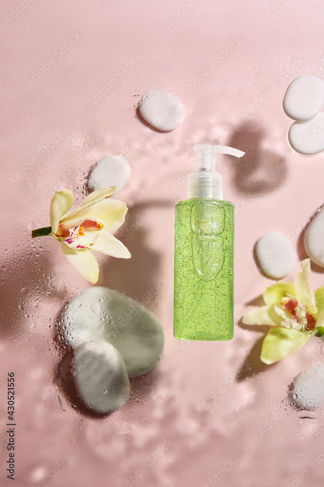 Bottle of cosmetic product and flower on glass with water drops