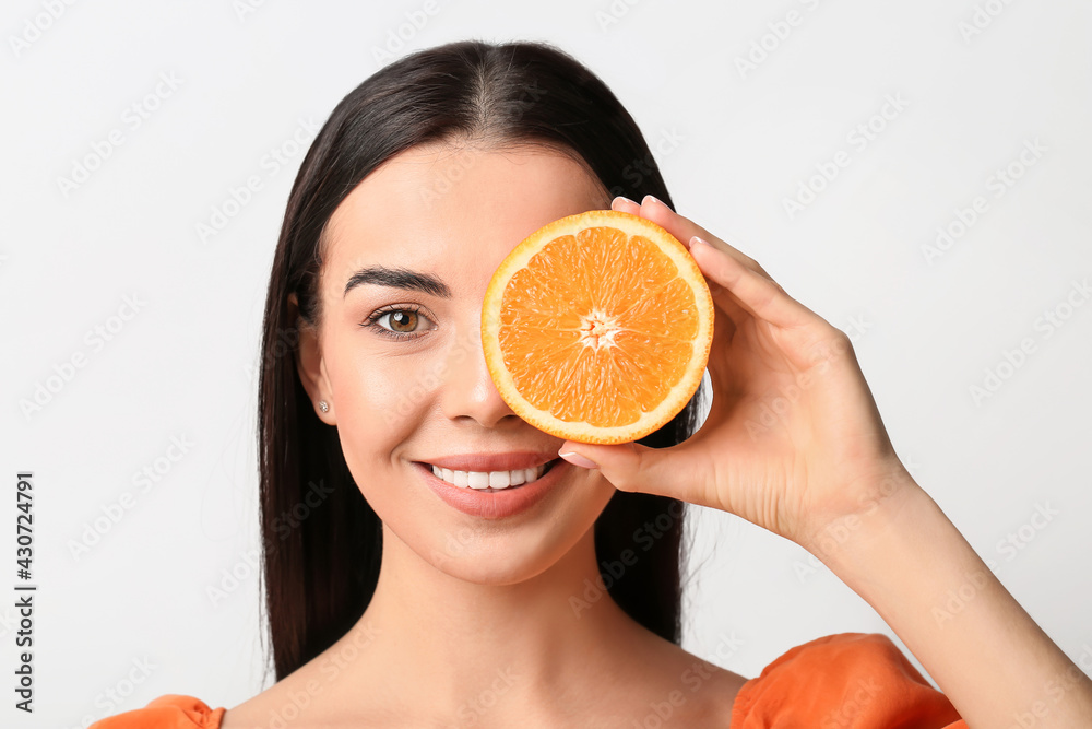 Beautiful young woman with orange on light background