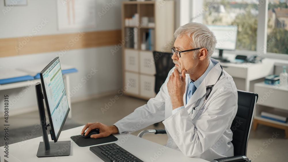 Experienced Middle Aged Male Doctor Wearing White Coat Working on Personal Computer at His Office. S