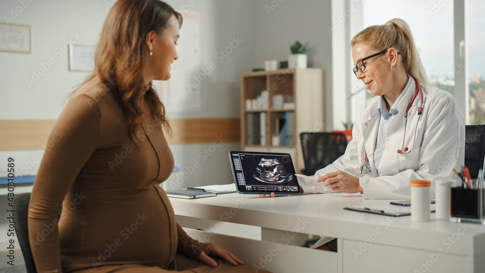 Female Physician Showing Tablet Computer with Ultrasound Pregnancy Scan to Young Future Mother Patie