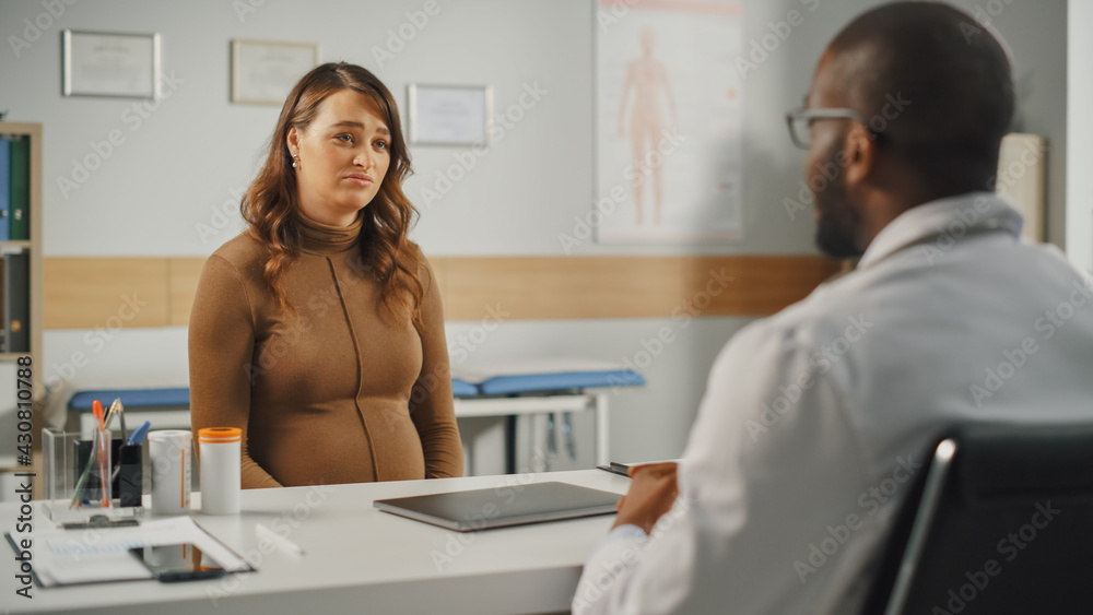 African American Family Doctor is Talking with Young Pregnant Patient During Consultation in a Healt