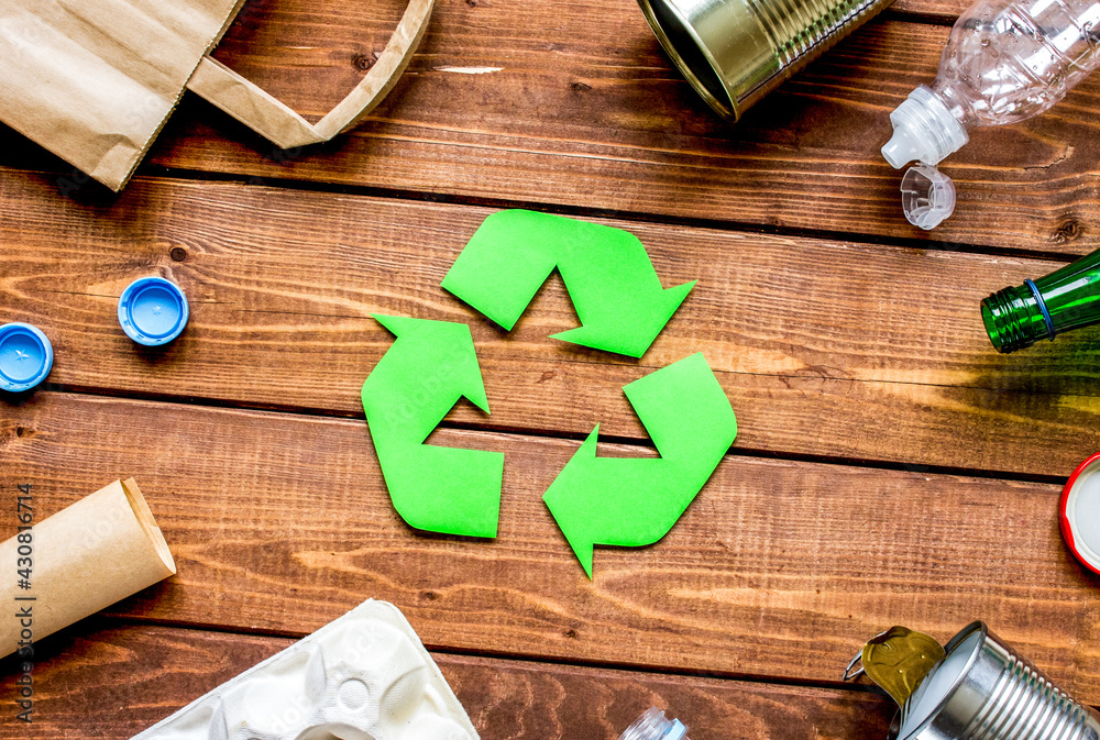 waste recycling symbol with garbage on wooden background top view