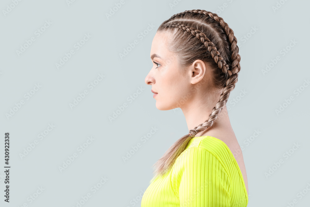 Beautiful young woman with braided hair on grey background