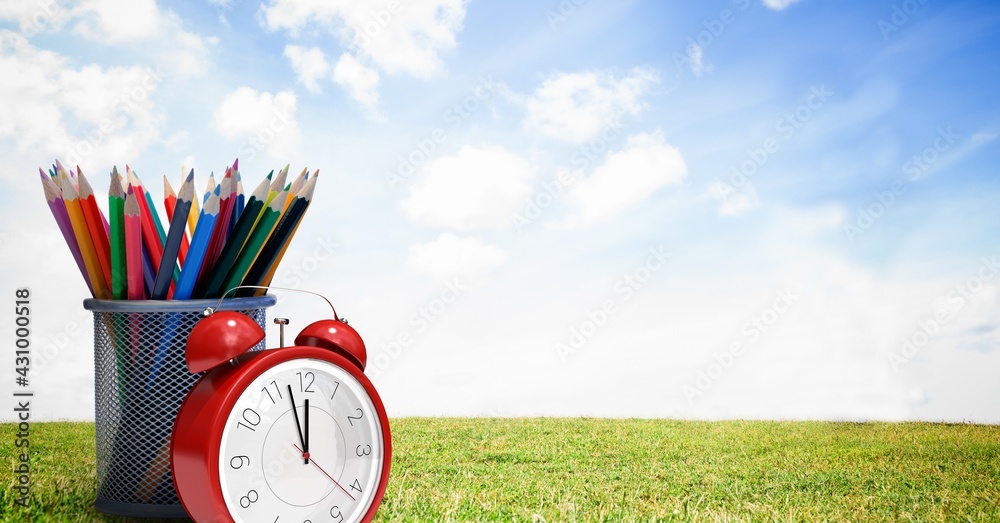 Composition of alarm clock and container of colour pencils over grass and sky