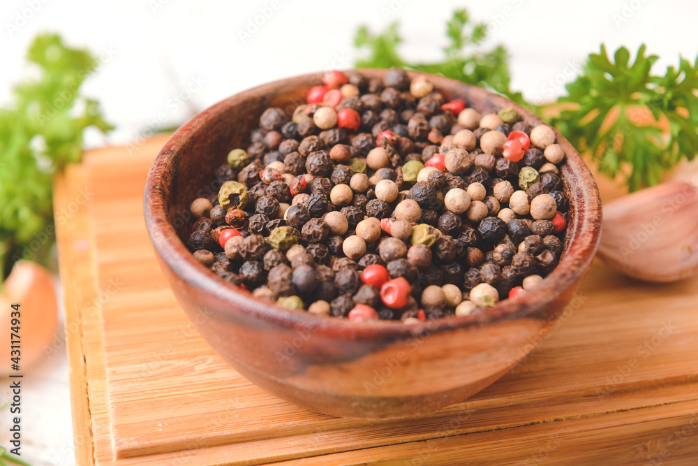 Bowl with peppercorns on light wooden background