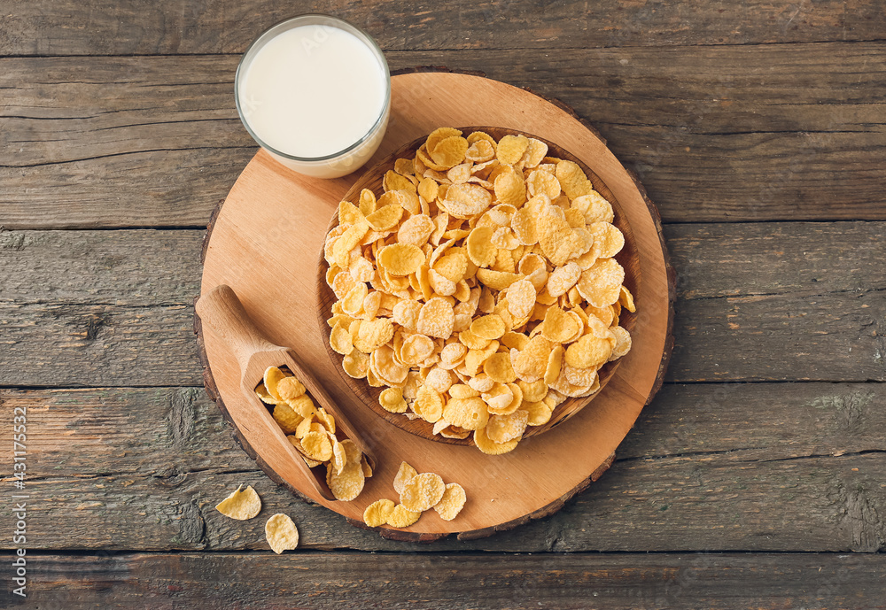 Glass of milk, plate and scoop with tasty cornflakes on wooden background