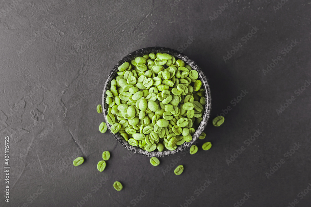 Bowl with green coffee beans on dark background