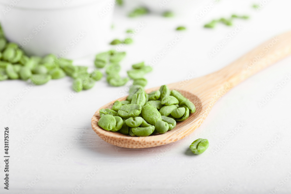 Spoon with green coffee beans on light background