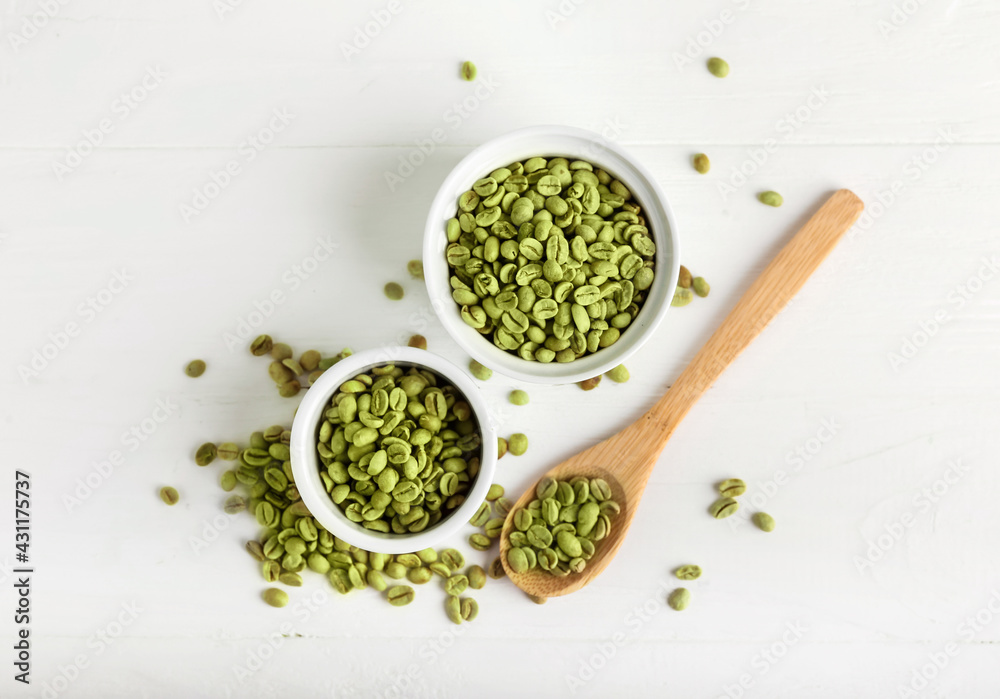 Bowls and spoon with green coffee beans on light background