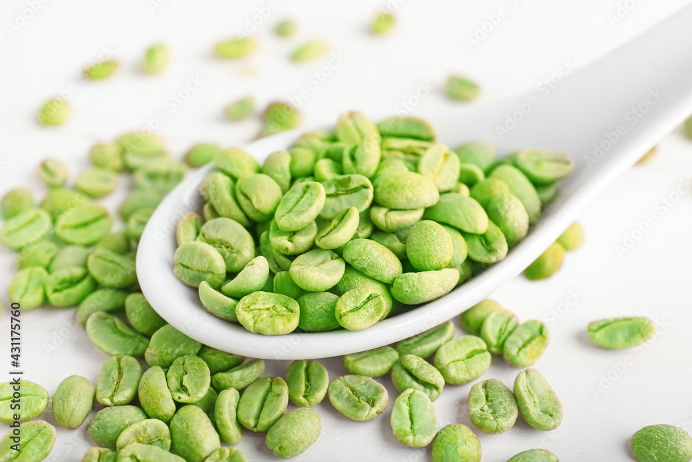 Spoon with green coffee beans on light background, closeup