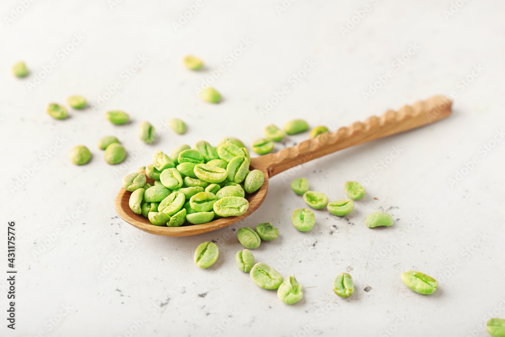 Spoon with green coffee beans on light background