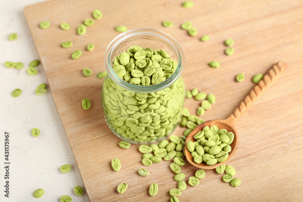 Jar with green coffee beans on wooden background